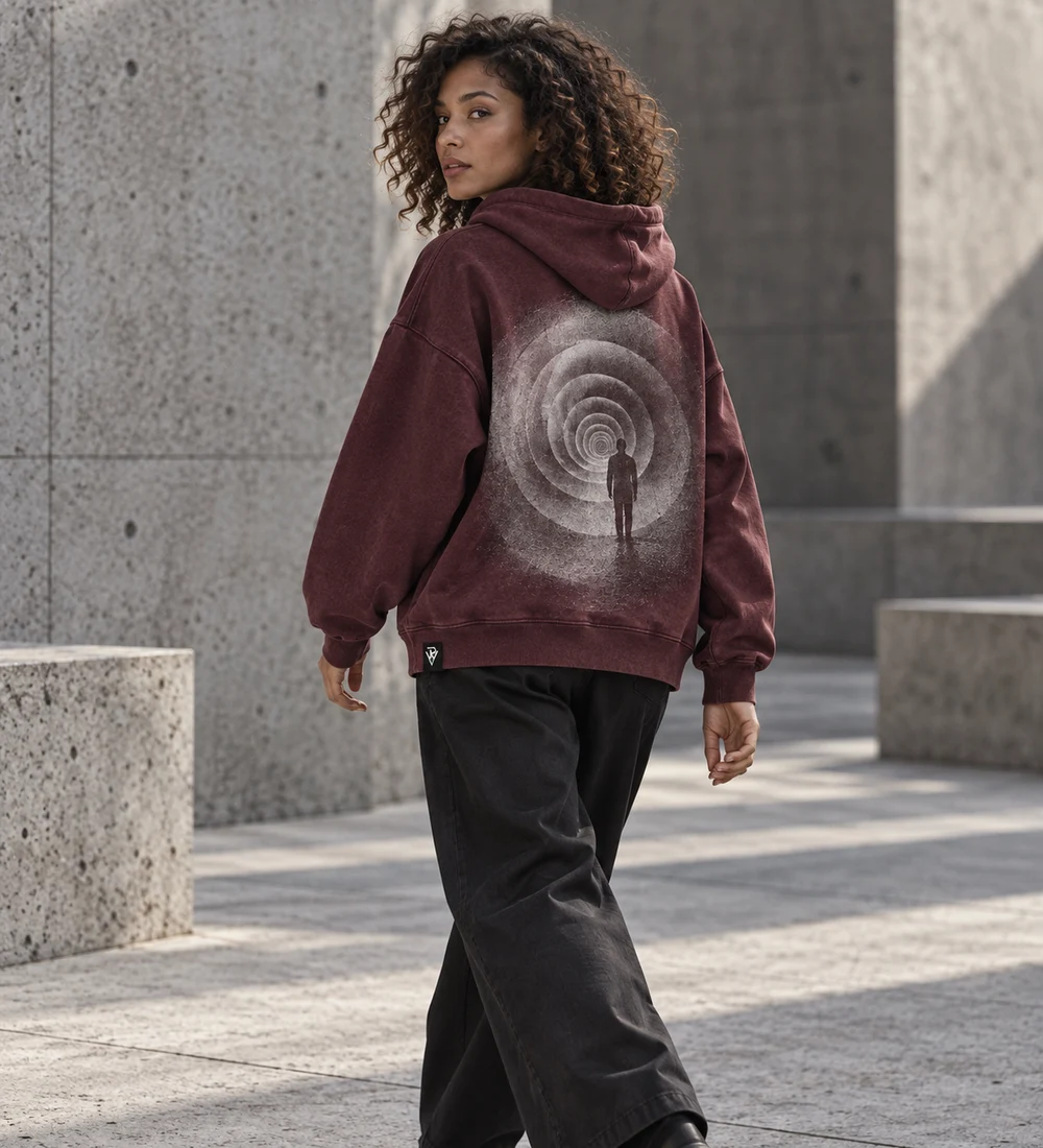 Adult female model walking in a burgundy oversized PRESENCE hoodie with concentric ring back artwork
