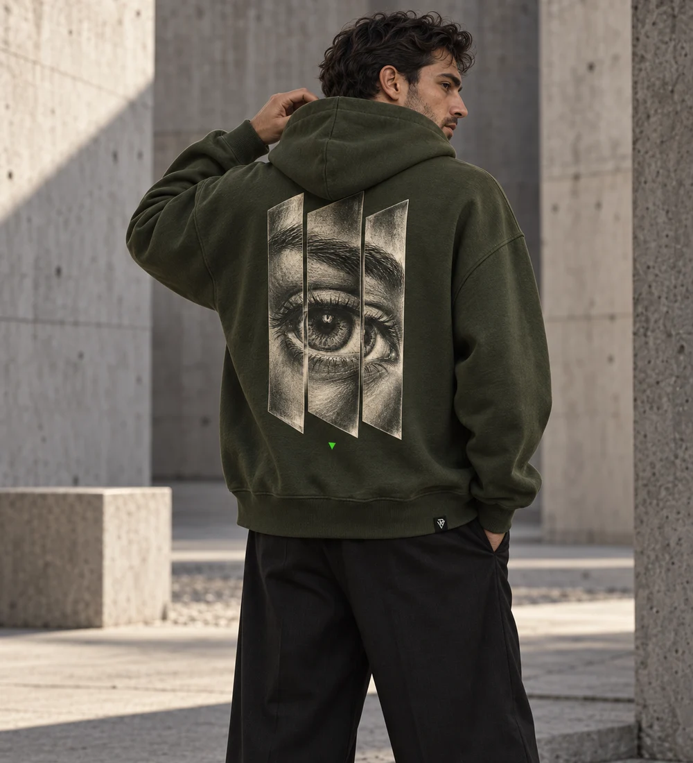 Adult male model wearing a deep-olive oversized REFRACTION hoodie with an etched eye split into three planes on the back