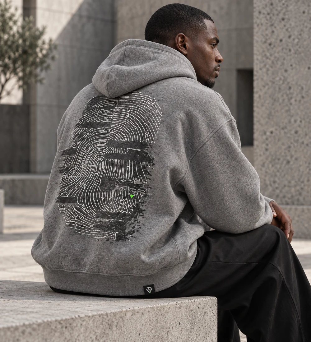 Adult male model seated in an ash-grey oversized TRACE hoodie with fingerprint back artwork